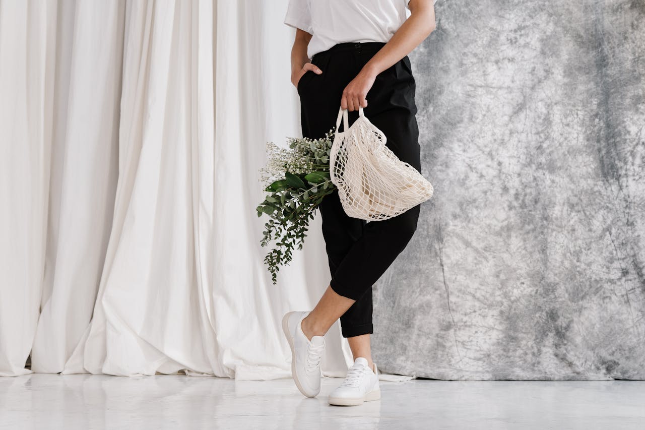 about-us-02 Adult holding eco-friendly mesh bag with green foliage against minimalist backdrop.